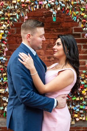 Couple gazing lovingly at each other framed by colorful padlock arch on brick wall.