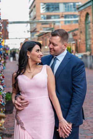 Elegant couple holding hands and smiling beside colorful love lock installation at distillery.