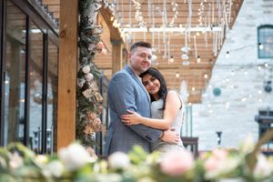 Happy couple embracing warmly under string lights and floral decor in a cozy outdoor venue.