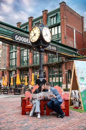 Couple kissing on a red bench beneath a clock tower outside Gooderhams historic building.