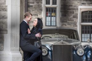 Couple in formal attire share a romantic moment leaning against a classic vintage Rolls-Royce.