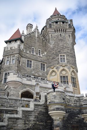 Couple embracing on the grand stone staircase of a majestic Gothic Revival castle.