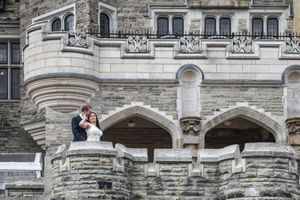 Bride and groom share a romantic kiss on the ornate stone balcony of a historic castle.