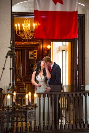 Couple kissing on an ornate balcony beneath a Canadian flag in a grand interior.