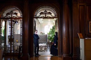 Two people standing in an elegant wood-paneled doorway with decorative arched details.