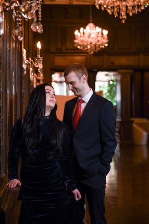 Couple in elegant evening wear share a romantic moment in a luxurious chandelier-lit hall.