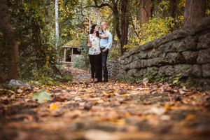 Couple walking hand in hand along a leaf-covered autumn path beside a stone wall.