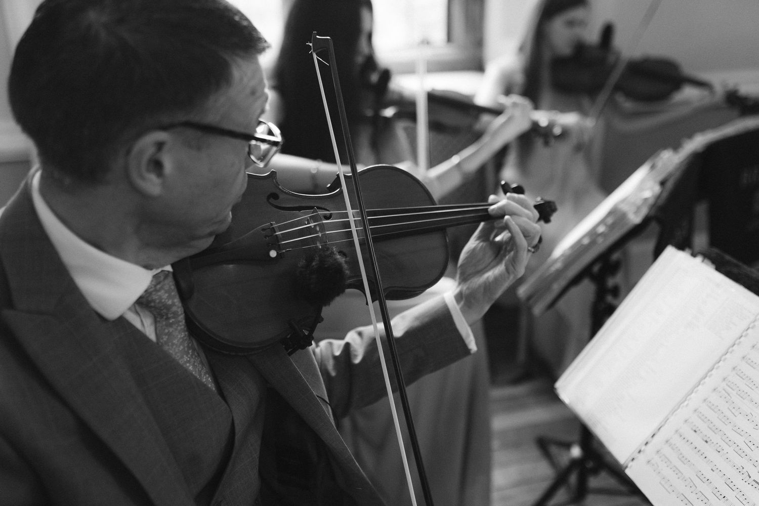 Black and white photo of a man in a suit playing violin while reading sheet music on a stand.