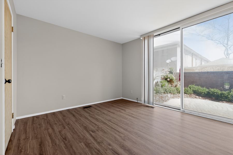 Empty room with dark hardwood floors, gray walls, and large sliding glass door leading to a patio with garden views.