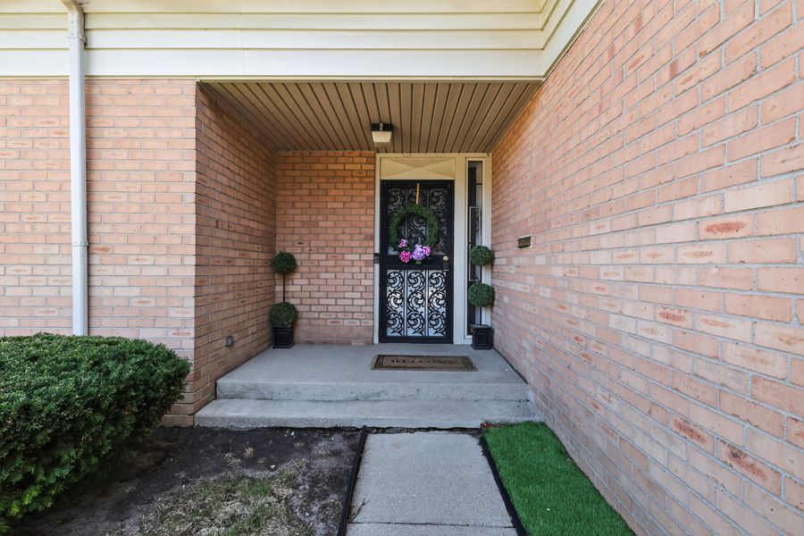 Brick home entryway with decorative wrought iron front door, topiary plants, and covered porch.
