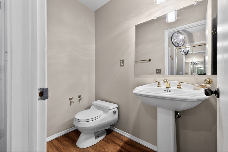 Clean powder room with pedestal sink, large mirror, white toilet, and wood-look flooring in neutral tones.