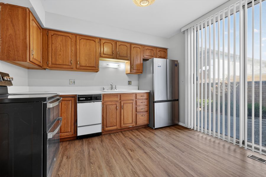 Kitchen with wooden cabinets, stainless steel refrigerator, white dishwasher, hardwood floors, and sliding glass door.
