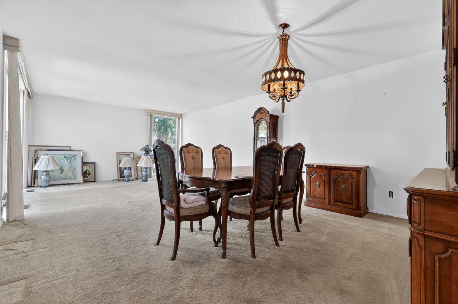 Elegant dining room with wooden table, upholstered chairs, chandelier, grandfather clock, and carpet flooring.