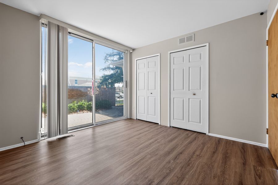 Bright empty bedroom with sliding glass door, two white closets, and dark hardwood floors.