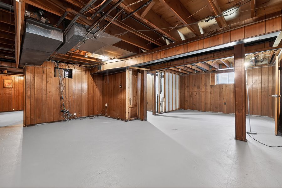 Unfinished basement with wood-paneled walls, painted concrete floors, and exposed ceiling joists.