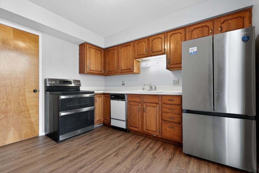 Kitchen with oak cabinets, hardwood floors, stainless steel fridge, and black electric range.