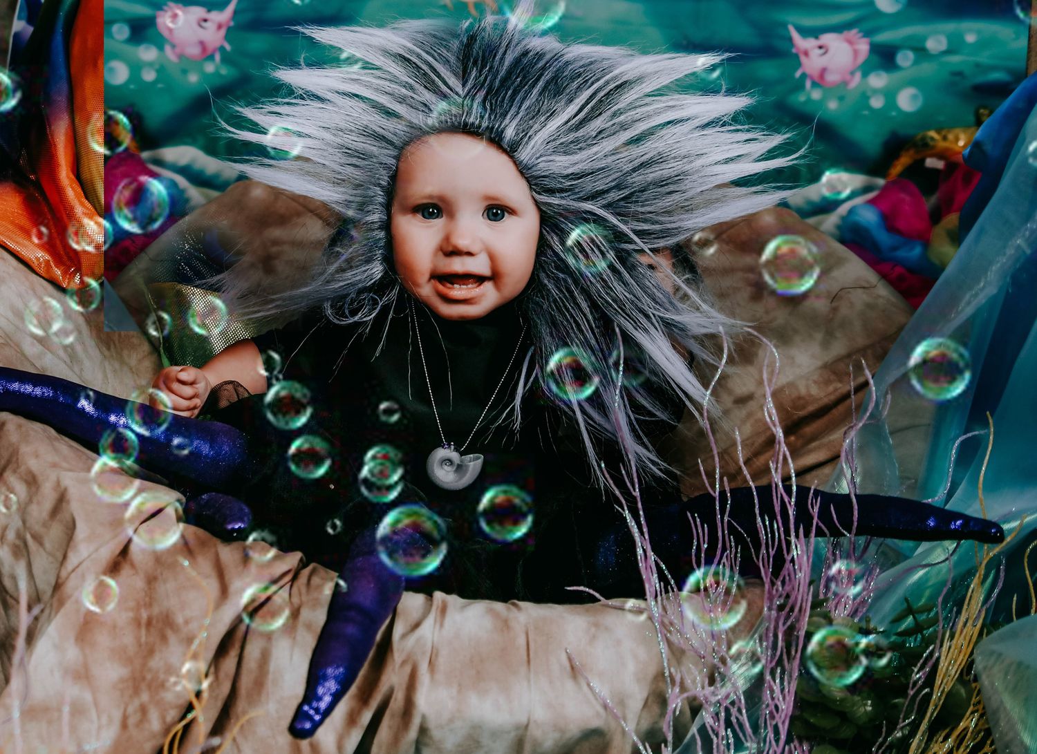 A baby in a whimsical costume with wild hair surrounded by colorful bubbles at a fantasy-themed event.