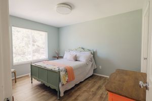 Bright bedroom with sage green walls, green metal bed frame, hardwood floors, and a large window letting in natural light.