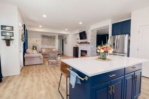 Navy blue kitchen island with white countertop, gold hardware, and view into cozy living room with fireplace.