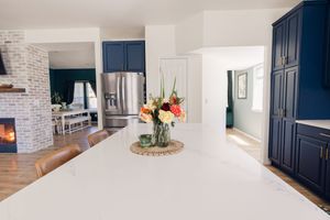 Modern kitchen with navy blue cabinets, white quartz island, stainless steel fridge, and fresh floral centerpiece.