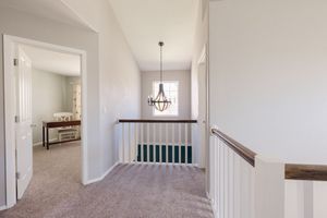 Bright upstairs hallway with carpet, white railings, and elegant chandelier over staircase.