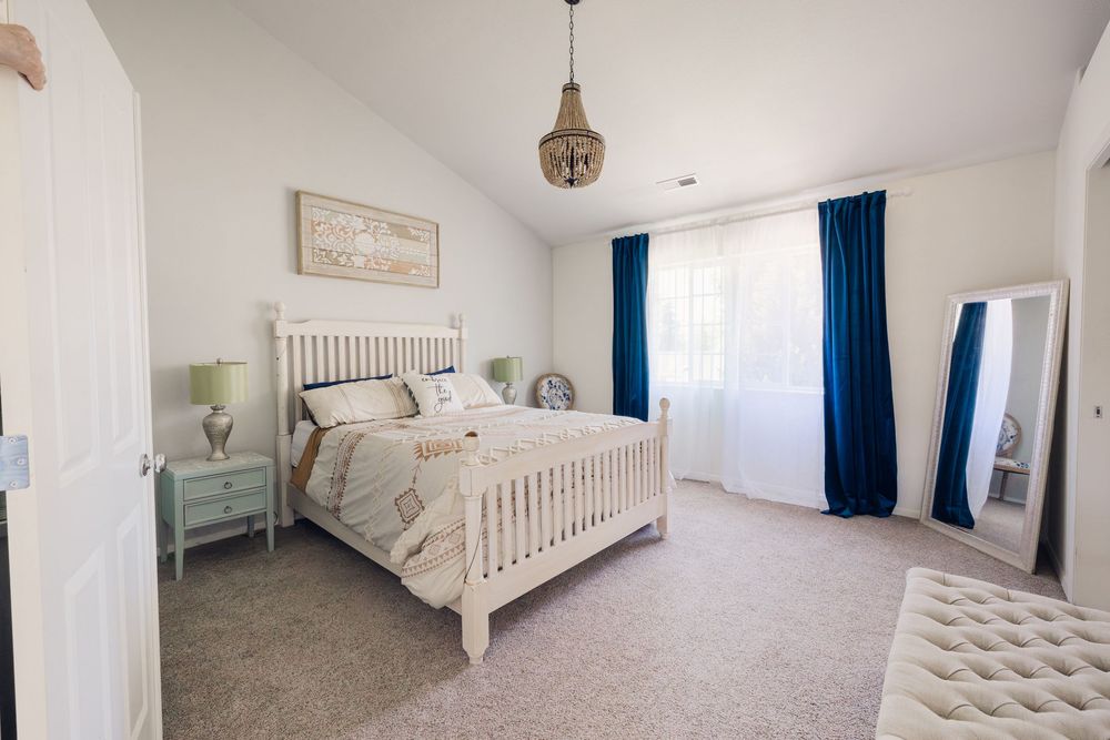Bright bedroom with white wood bed, blue curtains, pendant light, mint nightstand, and full-length mirror on carpet floor.