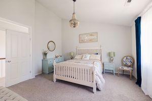 Bright bedroom with white wooden bed frame, pastel blue nightstands, chandelier, and neutral carpet.