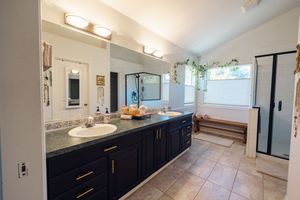 Modern bathroom with navy double vanity, granite countertops, large mirror, soaking tub, and tile floors.