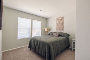 Cozy bedroom with gray bedding, carpeted floors, and natural light from double window.
