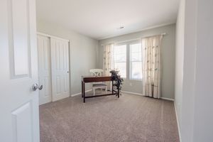 Bright spare bedroom with neutral carpet, white closet doors, and a dark wood console table near a curtained window.