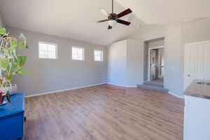 Spacious living room with vaulted ceiling, ceiling fan, hardwood floors, and large windows.