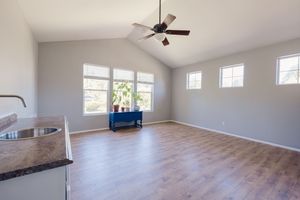 Bright open living room with vaulted ceiling, ceiling fan, hardwood floors, and large windows flooding the space with natural light.