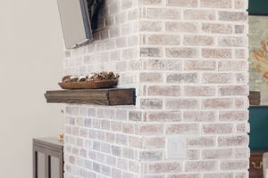 White-painted brick fireplace with rustic wood mantel shelf and decorative bowl in a modern living room.