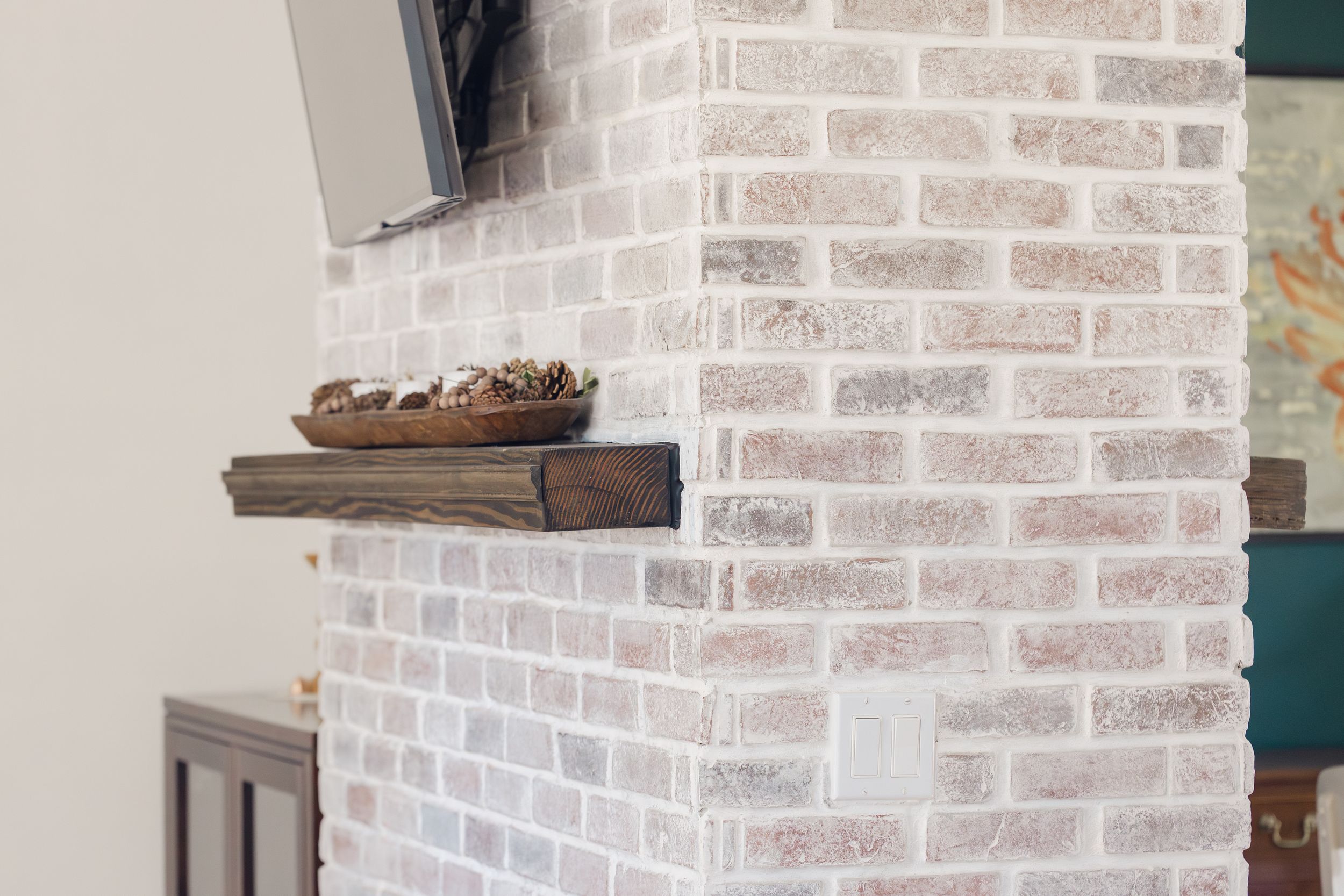 White-painted brick fireplace with rustic wood mantel shelf and decorative bowl in a modern living room.