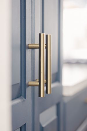 Gold brass bar pulls on navy blue shaker cabinet doors in a modern kitchen interior.