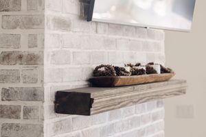 Whitewashed brick fireplace with rustic wooden mantel decorated with pinecones in a tray.