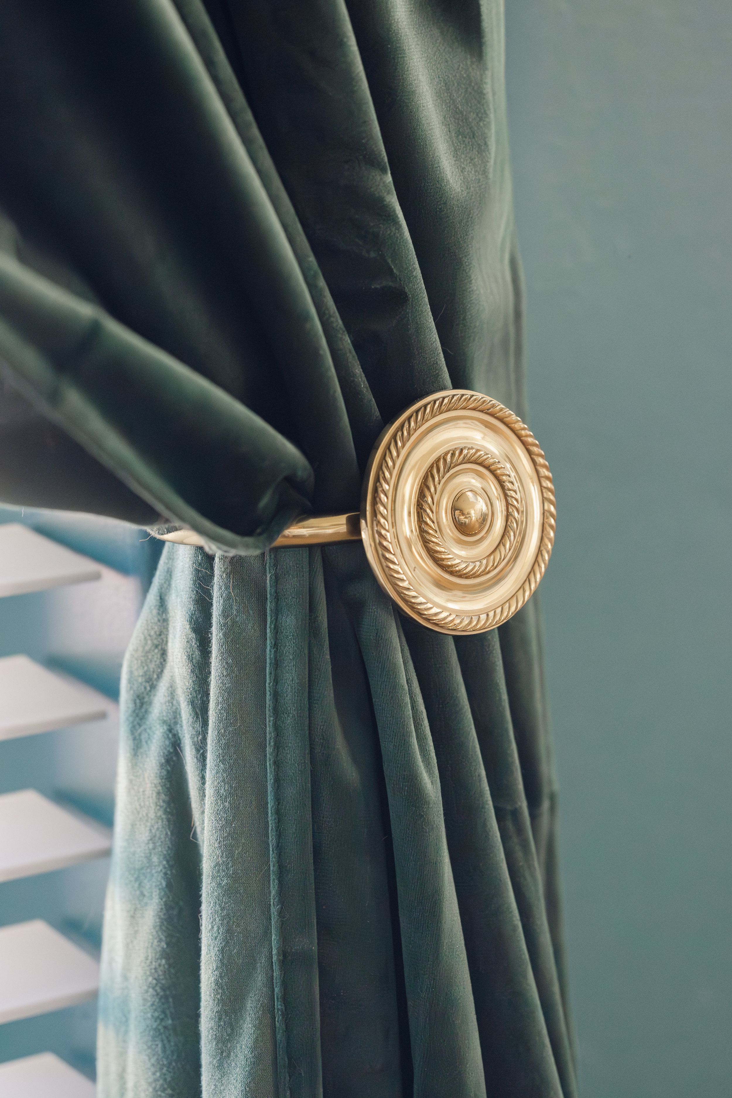 Elegant teal velvet curtain tied back with ornate gold circular curtain holdback.