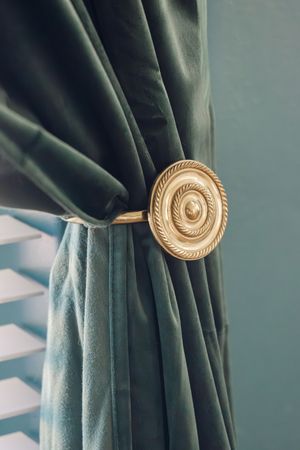 Elegant teal velvet curtain tied back with ornate gold circular curtain holdback.