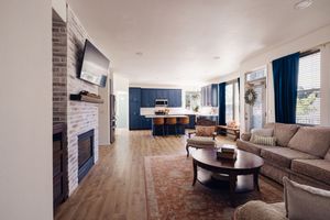 Open-concept living room with brick fireplace, hardwood floors, and blue kitchen cabinets.