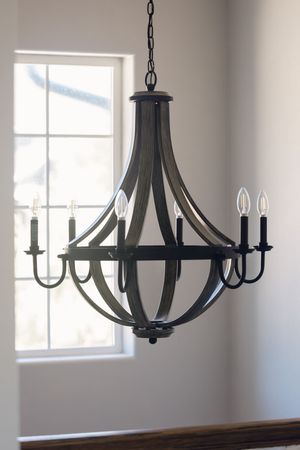 Black metal and wood barrel chandelier with candle lights hanging near staircase window.
