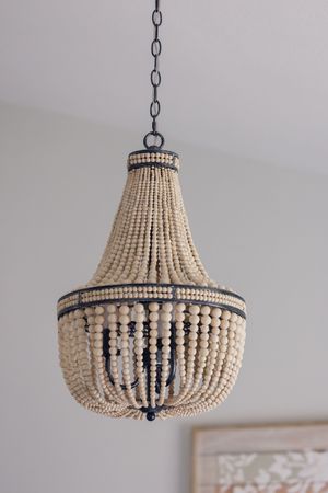 Elegant beaded chandelier with cream wooden beads and dark metal frame hanging from a white ceiling.
