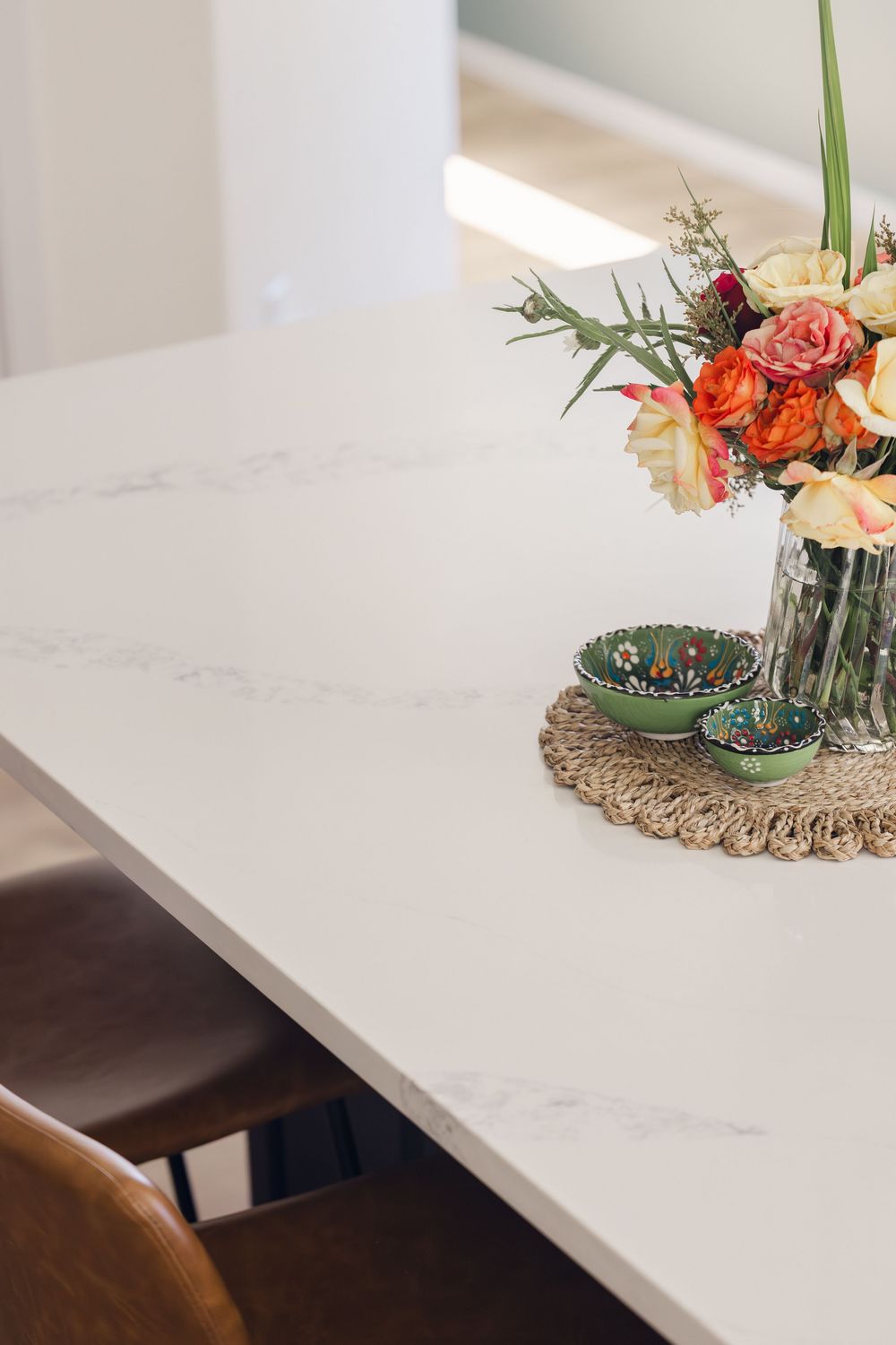 White marble countertop with fresh floral arrangement and decorative green bowls on woven mat.