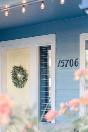 Blue house exterior with white trim, wreath on door, string lights, and address number 15706.