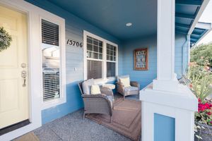 Charming blue house front porch with wicker chairs, yellow door, and number 13706 in a sunny neighborhood.