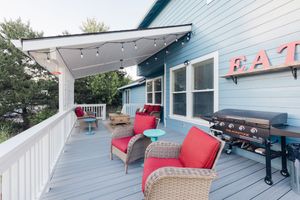 Outdoor deck with red cushioned chairs, string lights, and a grill on a blue house patio.