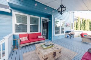 Spacious blue covered porch with red cushioned sofa, wicker chairs, and rustic coffee table.