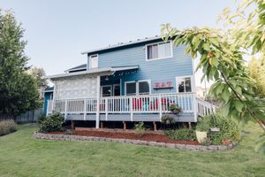 Blue two-story craftsman home with white deck, manicured lawn, and cherry tree in foreground.