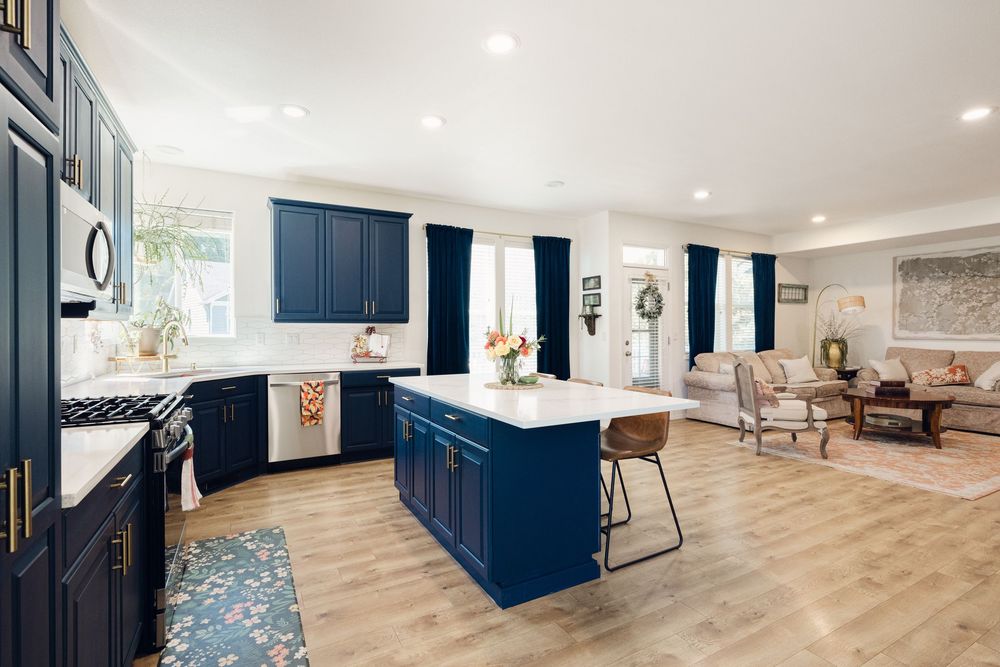 Modern kitchen with navy blue cabinets, white quartz island, stainless appliances, and open living area.