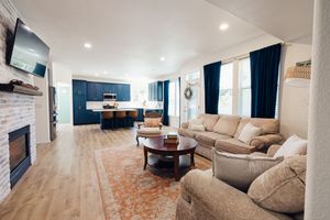 Tri-Cities Bright open-concept living room with beige sofas, brick fireplace, hardwood floors, and navy blue kitchen cabinets in background.