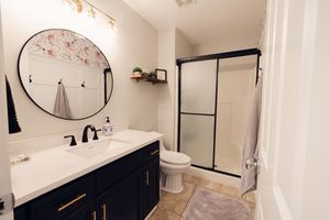 Modern bathroom with navy vanity, round mirror, walk-in shower, and neutral tile flooring.